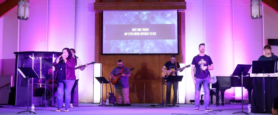 Church worship team sings and plays music on stage while song lyrics are projected behind them